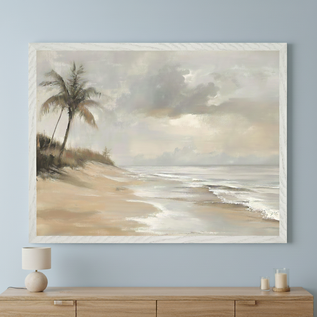 Modern living room with a light wood dresser. A large framed painting of a muted beach scene with palm trees, sandy shore, and a cloudy sky hangs centered above the dresser. A table lamp and candles sit on the dresser.