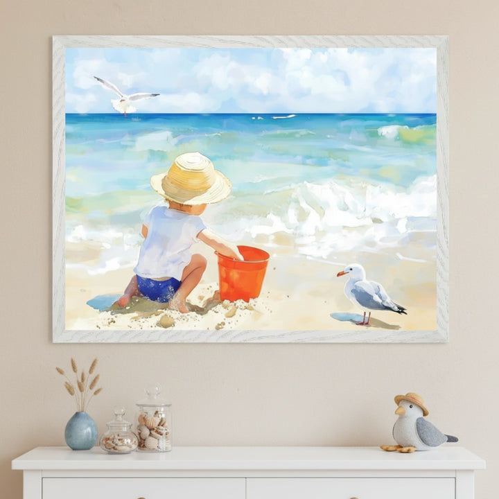 A child kneels on the beach facing the ocean, wearing a straw hat and playing with a red bucket in the sand, while a seagull watches close by. The framed painting hangs above a dresser with soft coastal decorations, evoking a peaceful seaside scene.