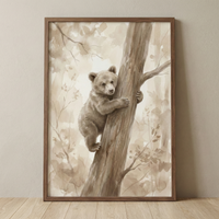A sepia-toned watercolor illustration of a young bear cub climbing a tree trunk. The cub, with fluffy fur and small ears, looks towards the viewer while clinging to the wood. The background shows a soft-focus forest with blurred leaves and branches in a monochrome beige palette. The artwork is presented in a slim wooden frame, resting on a light-colored floor against a plain wall.