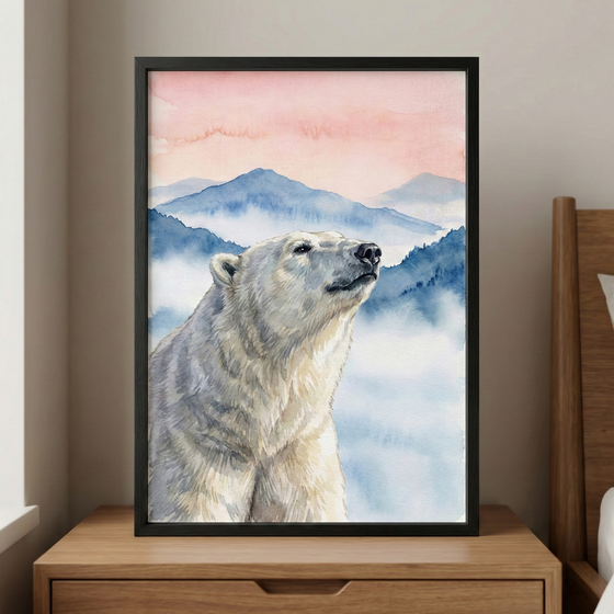 A serene watercolor-style illustration of a polar bear is displayed in a slim black frame. The bear is shown from the shoulders up, looking upward and to the side with a calm expression. Its fur is captured with soft washes of white, cream, and grey. Behind the bear, a landscape of rolling blue mountains rises into a soft pink and peach-colored sky, with white mist settled in the valleys. This framed artwork sits on a light-colored wooden nightstand next to a corner of a bed, creating a peaceful atmosphere.
