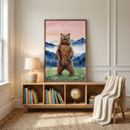 A large rectangular wooden frame hangs on a light-colored wall with classic architectural molding. The artwork inside features a brown bear standing on its hind legs in a meadow filled with small wildflowers. The background of the illustration depicts misty blue mountains beneath a soft sky with shades of pink and peach.

