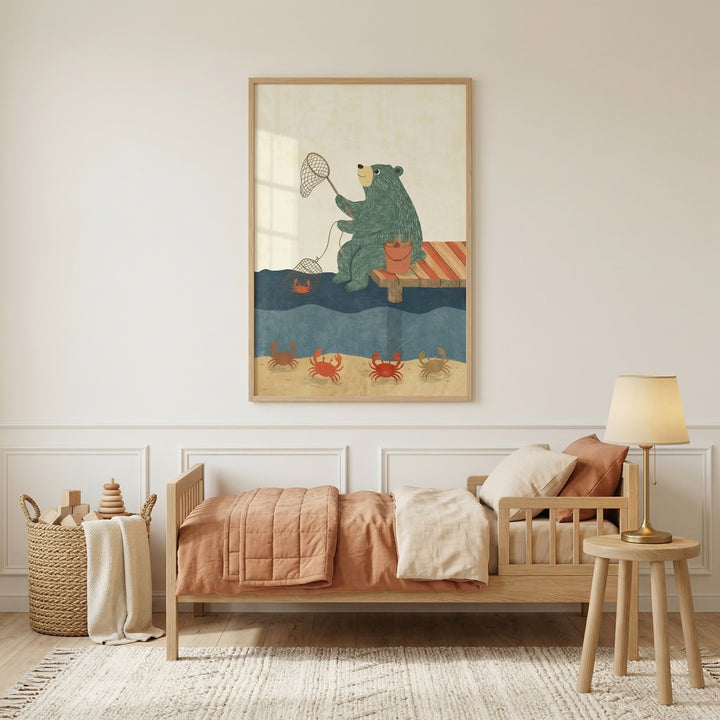 Large framed children’s illustration above a wooden toddler bed shows a green bear sitting on a dock holding crab nets over the water while red crabs move along the sandy seabed below. The artwork hangs in a cozy nursery with warm bedding, a woven toy basket, and a bedside lamp.