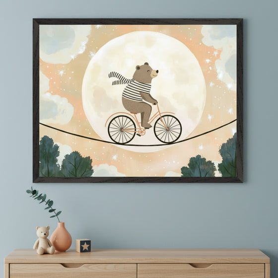 Kid's room with a light blue wall and a light wood dresser. A large framed print hangs centered above the dresser, depicting a cartoon bear in a striped shirt and scarf riding a bicycle on a tightrope across a full moon, with stars and trees, in a whimsical style.