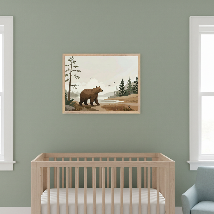Modern nursery with a wooden crib against a sage green wall. A framed illustration of a brown bear walking by a river with trees and mountains hangs centered above the crib. A light blue armchair is partially visible.