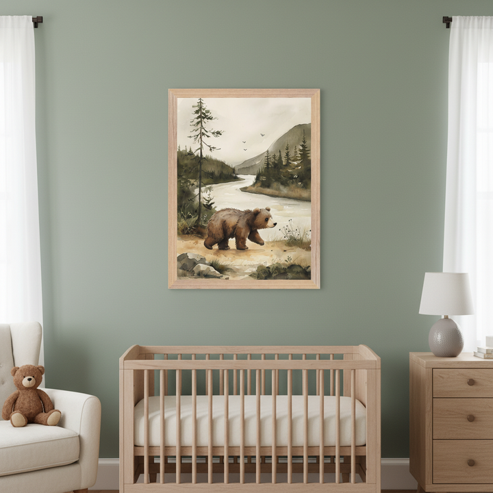 Modern nursery with a sage wall. A framed watercolor of a bear by a forest river hangs above a wood crib. A wood dresser with a lamp is to the right; a white armchair with a teddy bear to the left.