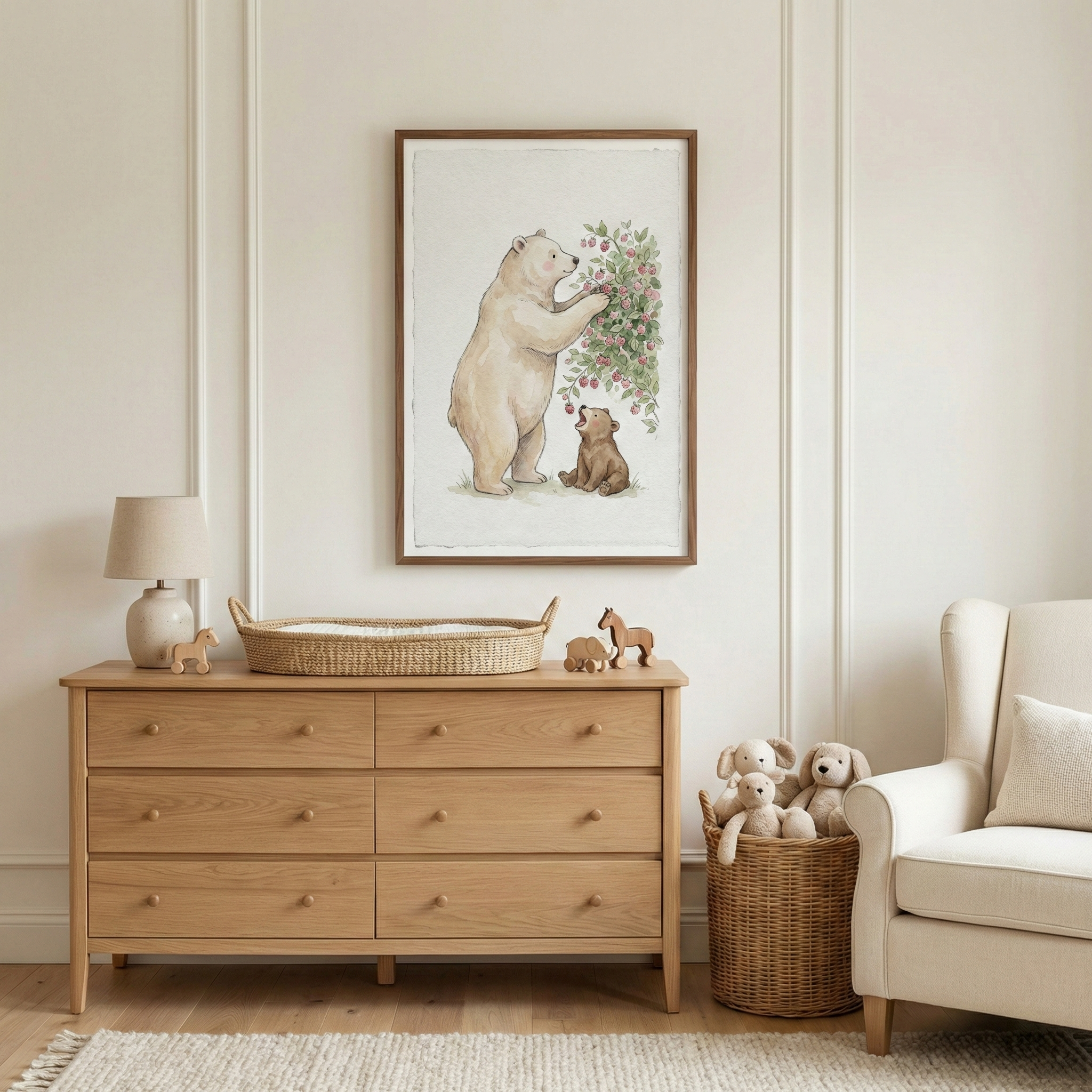 A serene nursery features a light wood dresser centered against a cream wall with classic molding. Above it hangs a large framed watercolor illustration of a light-colored bear and a small cub. The dresser is topped with a simple lamp, a woven changing tray, and wooden horse toys. To the right, a wicker basket holds plush toy dogs beside a cream armchair. The scene is completed with a light wood floor and a textured white area rug.