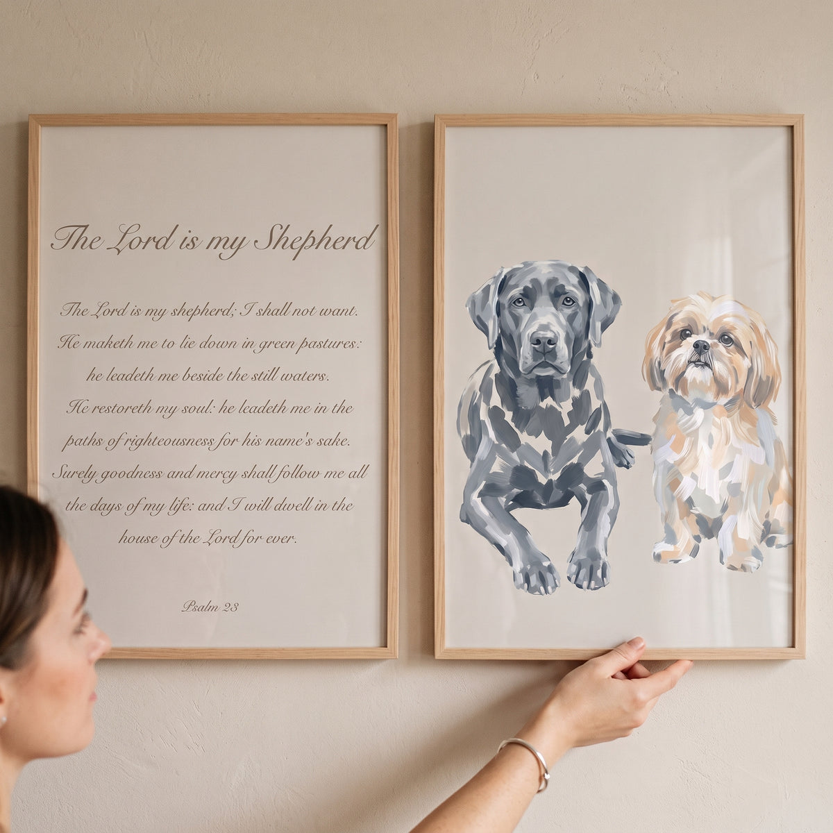 A woman displays a beige painterly psalm dogs wall art set of 2 with Psalm 23 text and two dog portraits on a wall.