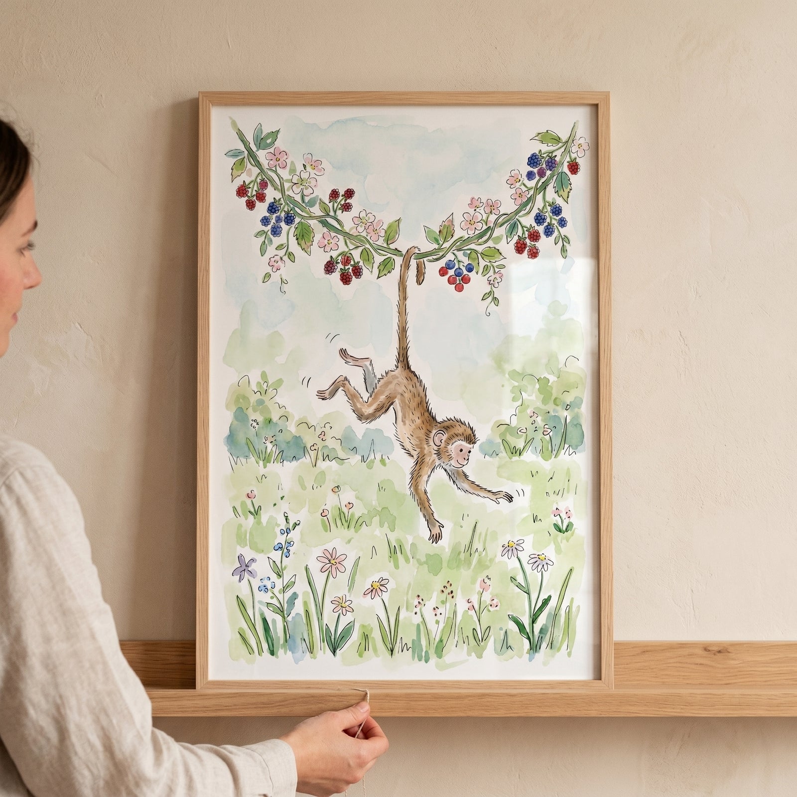 Watercolor berry vine hanging monkey wall art in a wooden frame on a shelf as a person adjusts it.
