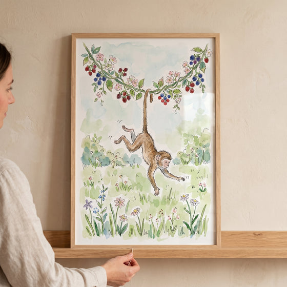 Watercolor berry vine hanging monkey wall art in a wooden frame on a shelf as a person adjusts it.