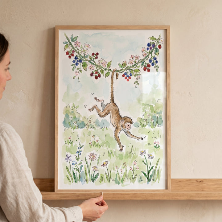 Watercolor berry vine hanging monkey wall art in a wooden frame on a shelf as a person adjusts it.