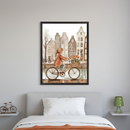 Bedroom with a grey upholstered bed and white pillow. A large framed watercolor print of a girl riding a bike with tulips in front of canal houses hangs centered above the bed.