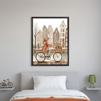 Bedroom with a grey upholstered bed and white pillow. A large framed watercolor print of a girl riding a bike with tulips in front of canal houses hangs centered above the bed.