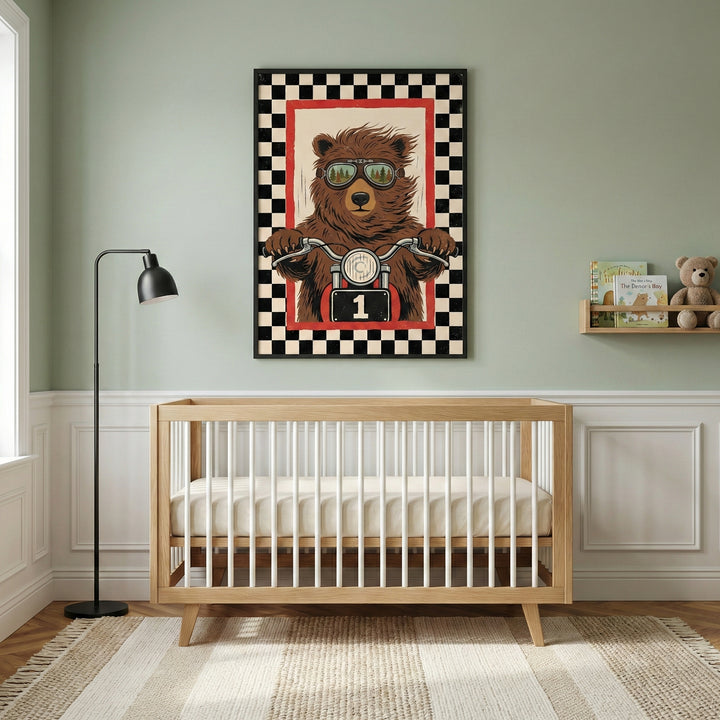 A bright nursery room with a wooden crib placed against a sage green wall. Above the crib, a large framed art piece depicts a brown bear wearing goggles and riding a motorcycle, surrounded by a red and black-and-white checkered border. To the left is a tall black floor lamp, and to the right is a small wall-mounted shelf holding a few books and a plush bear toy. The floor is light wood with a textured, neutral-toned rug.