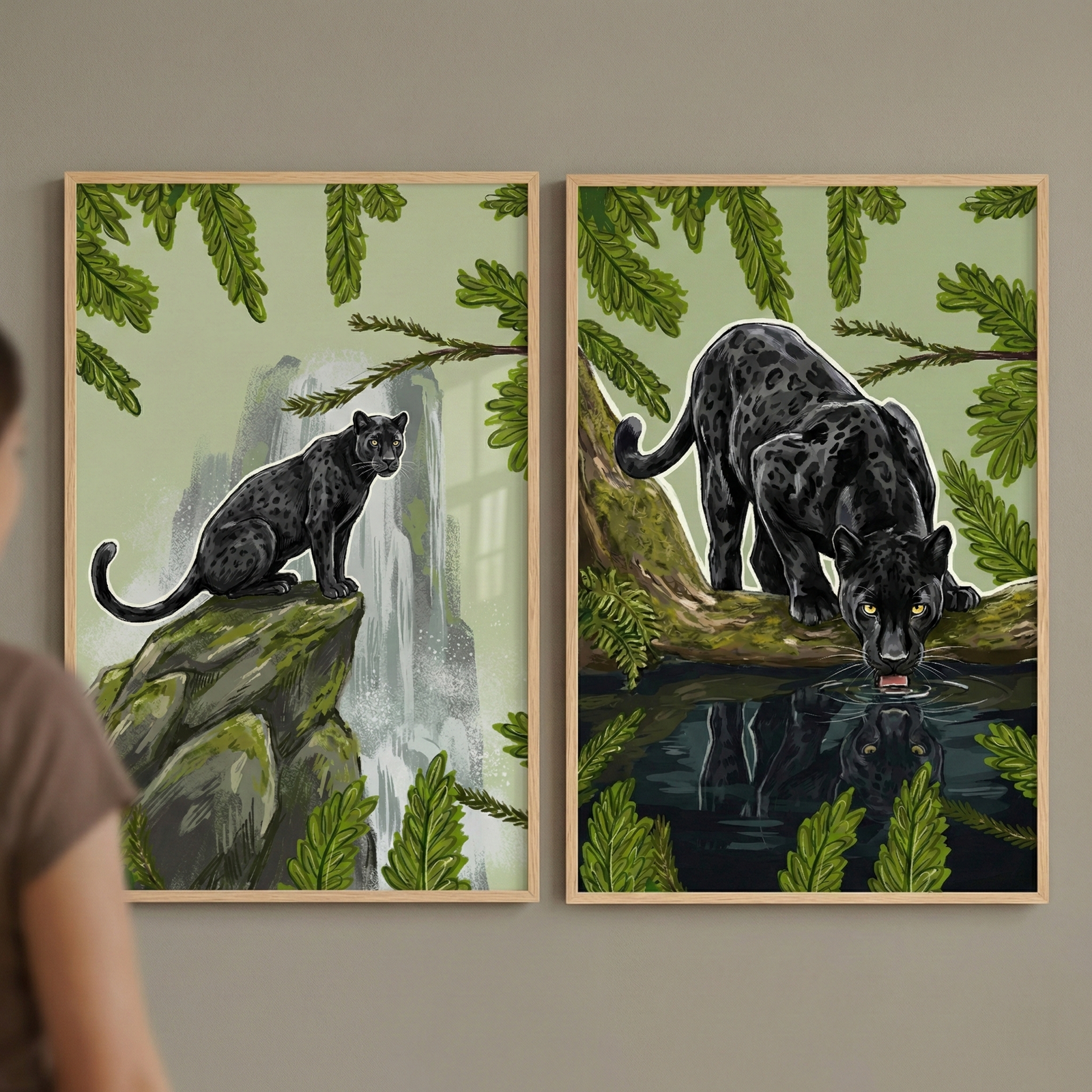 Two framed digital illustrations of black panthers are mounted on a neutral wall. In the left frame, a sleek jungle cat with subtle spots sits on a mossy rock formation in front of a misty waterfall. In the right frame, the panther is perched on a tree branch, leaning down to drink from a pool of water that shows its reflection. Both scenes feature lush green jungle foliage and a light-colored sky. The feline subjects have a white outline. A person is partially visible on the far left.