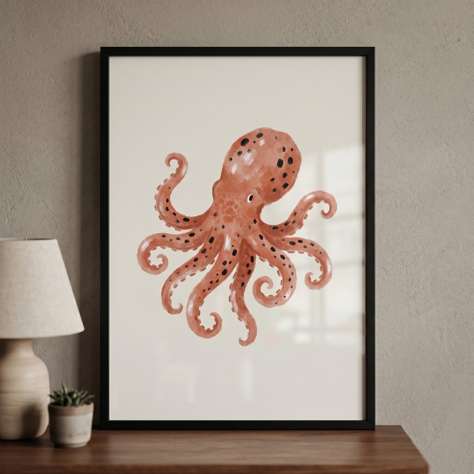 Framed black spotted rust octopus artwork on a wall next to a lamp and small potted plant on a wooden table.