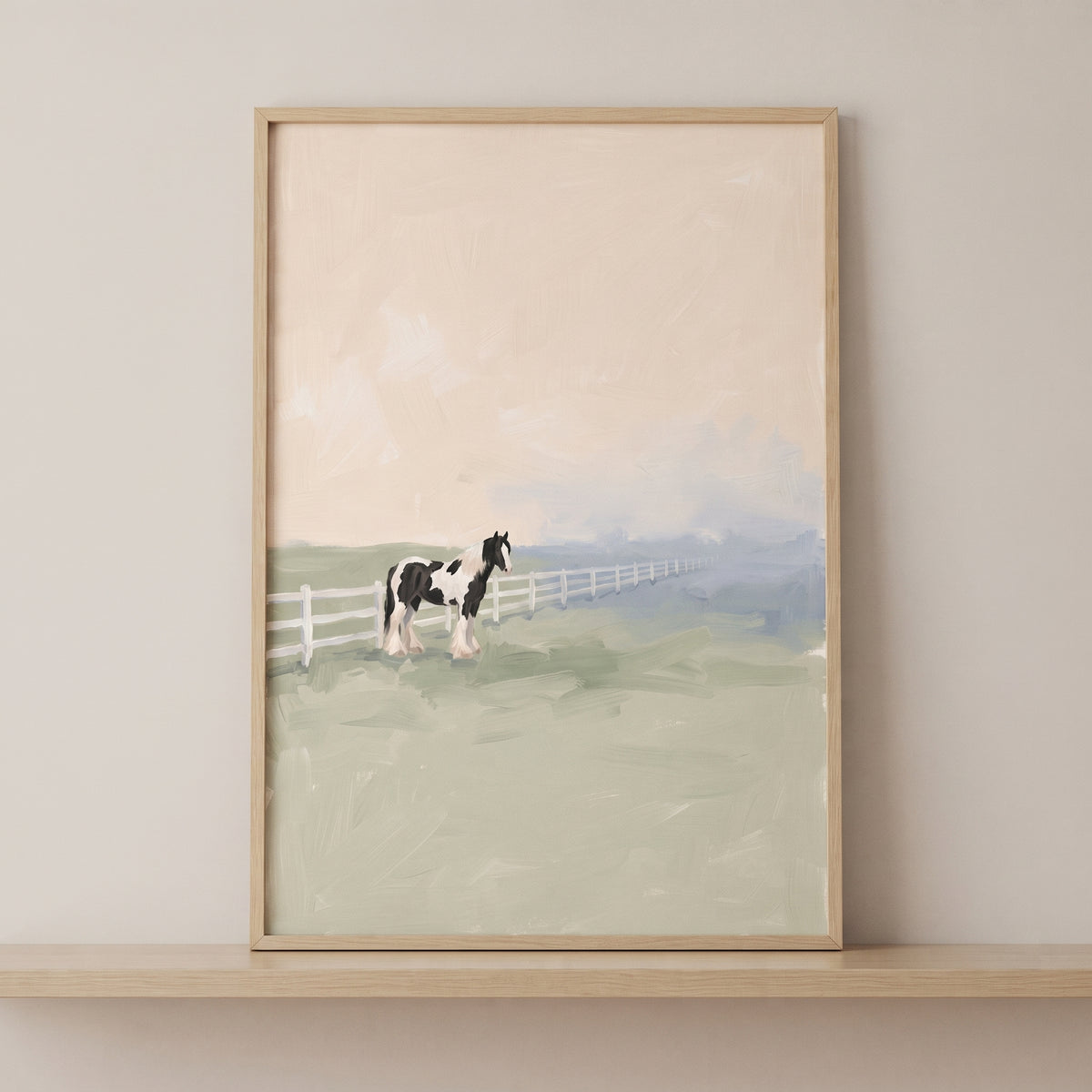Framed black white pinto horse wall art displays a horse in a muted green field beside a white fence on a shelf.