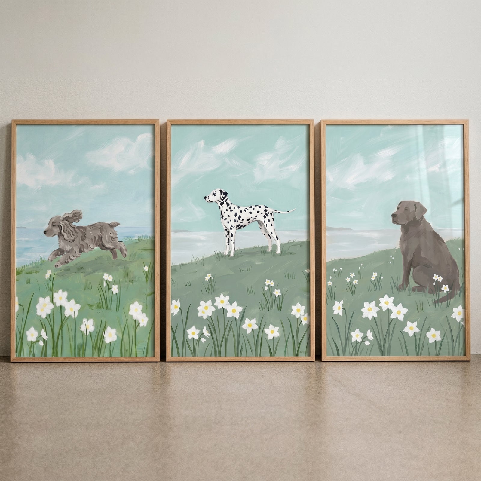 Blooming white daffodil dogs wall art set of 3 depicts three dogs in grassy meadows with white flowers and a blue sky.