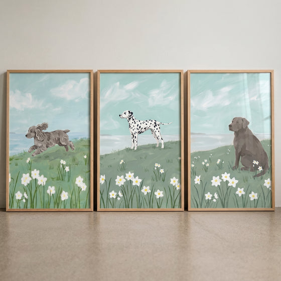 Blooming white daffodil dogs wall art set of 3 depicts three dogs in grassy meadows with white flowers and a blue sky.