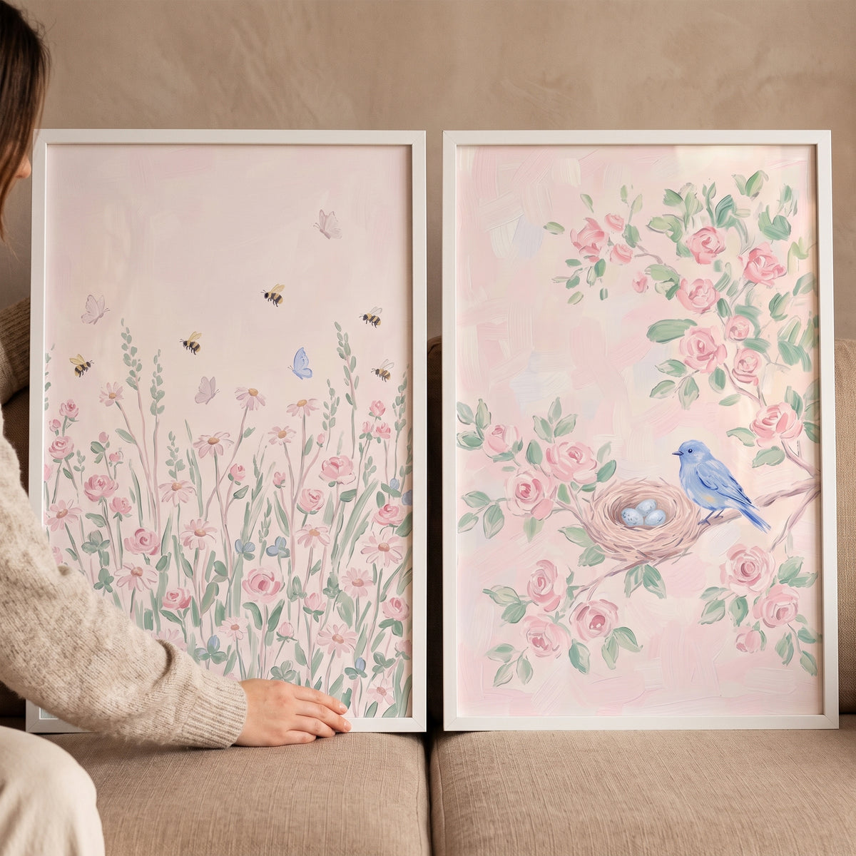 A hand holds a blossom blush nature garden wall art set of 2 with a blue bird, nest, and pink flowers in white frames.
