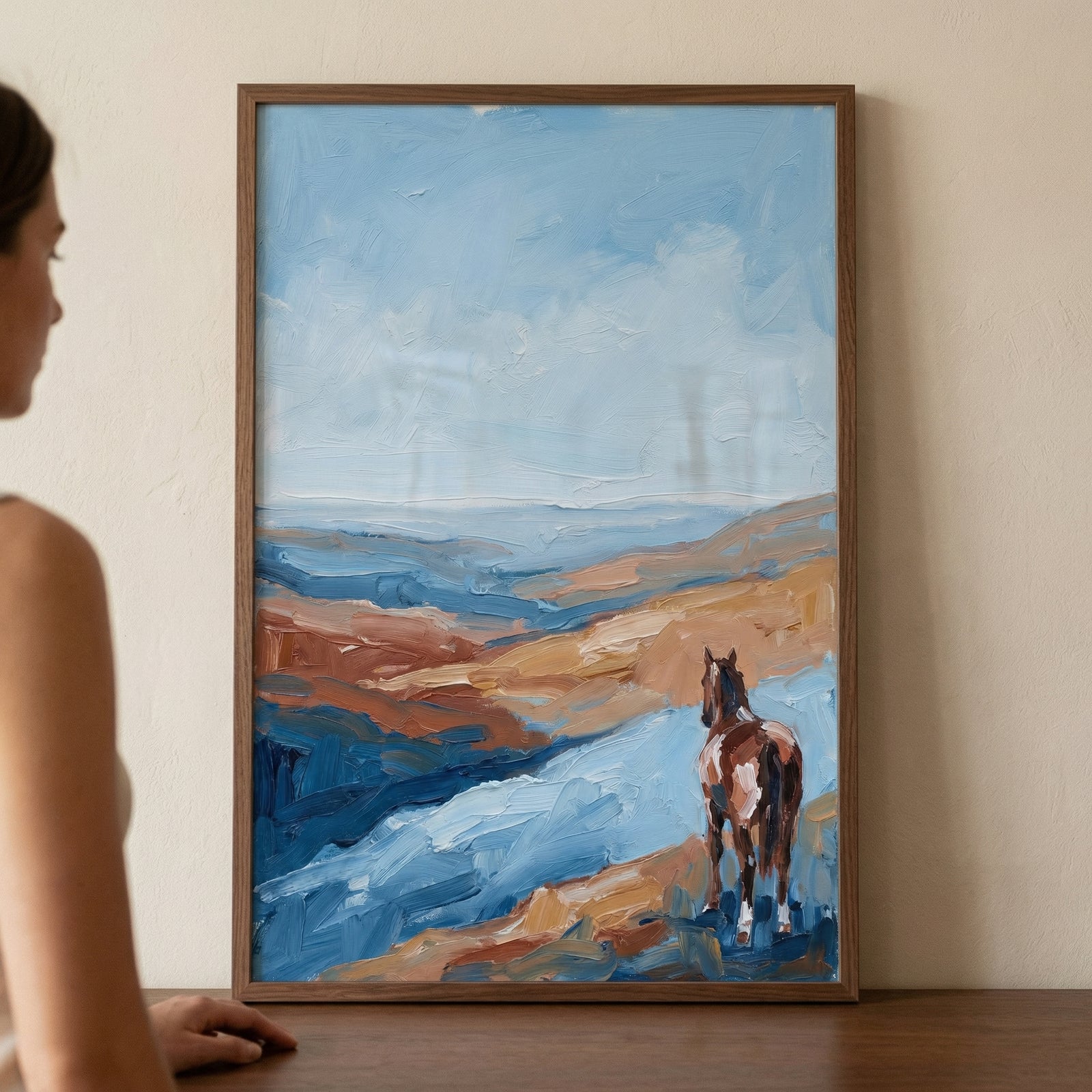 A rectangular artwork in a thin wooden frame hangs on a plain, neutral-toned wall. To the left, a person is partially visible in profile, appearing to gaze at the piece.
