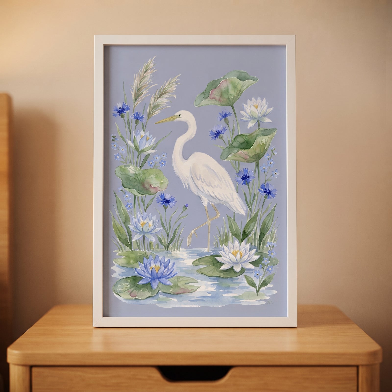Framed blue cornflower white egret bird wall art with water lilies sits on a wooden nightstand in a lit room.