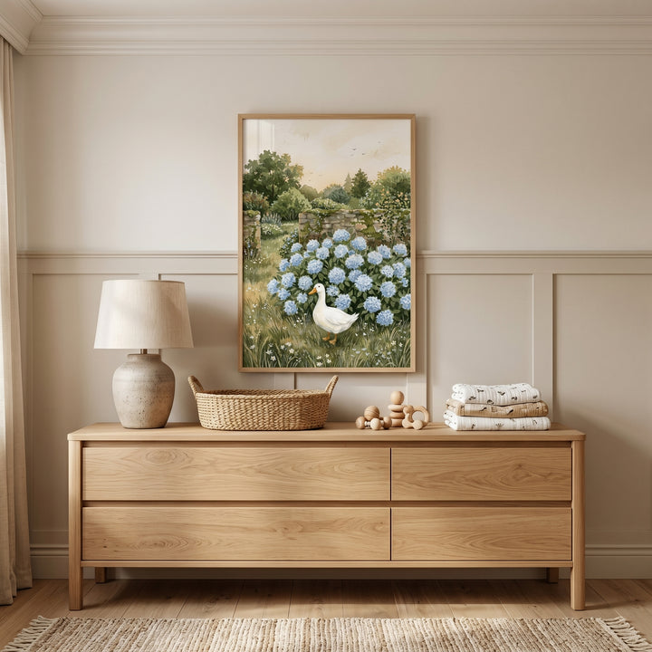 Blue flowers white duck wall art hangs above a wooden dresser with a lamp and wicker basket in a neutral nursery.