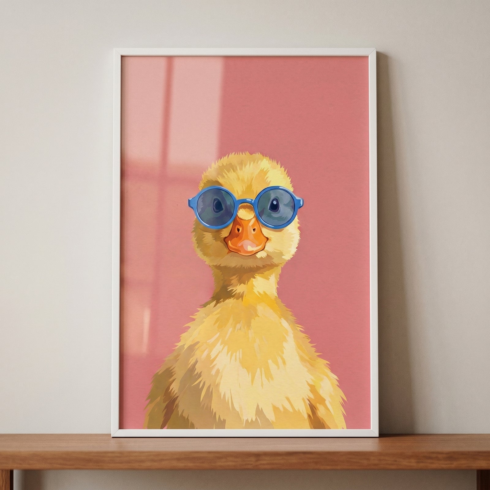 Framed blue glasses yellow duckling wall art featuring a cute duck on a pink background resting on a wooden shelf.