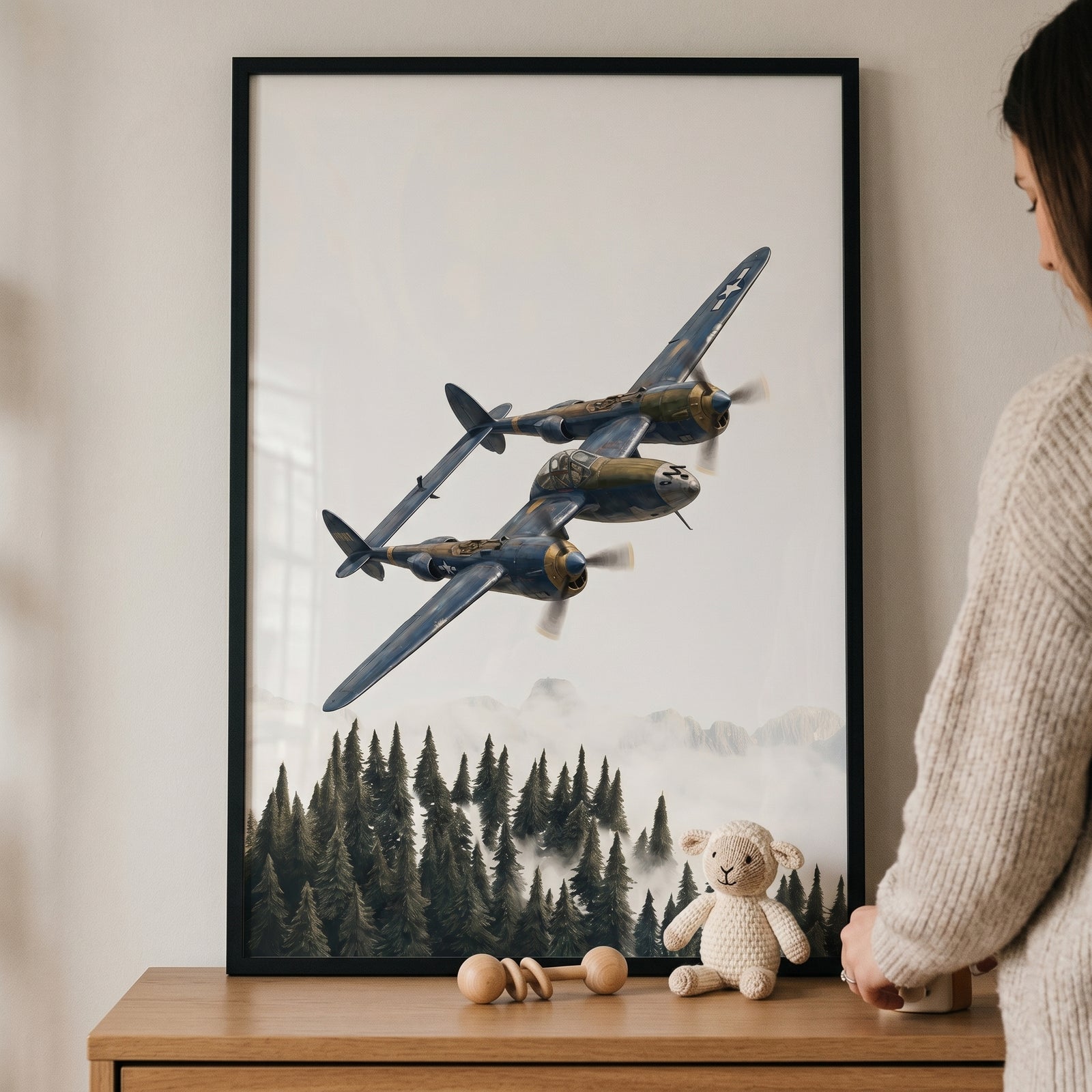 Framed blue gold vintage airplane wall art of a twin-boom plane over a forest on a nursery dresser with a toy lamb.