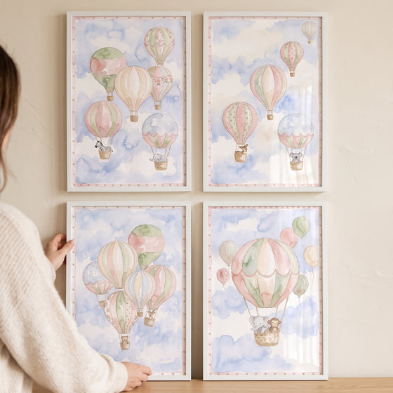 Person adjusting a blue hot air balloon wall art set of 4 featuring watercolor animals and clouds in a pastel sky.