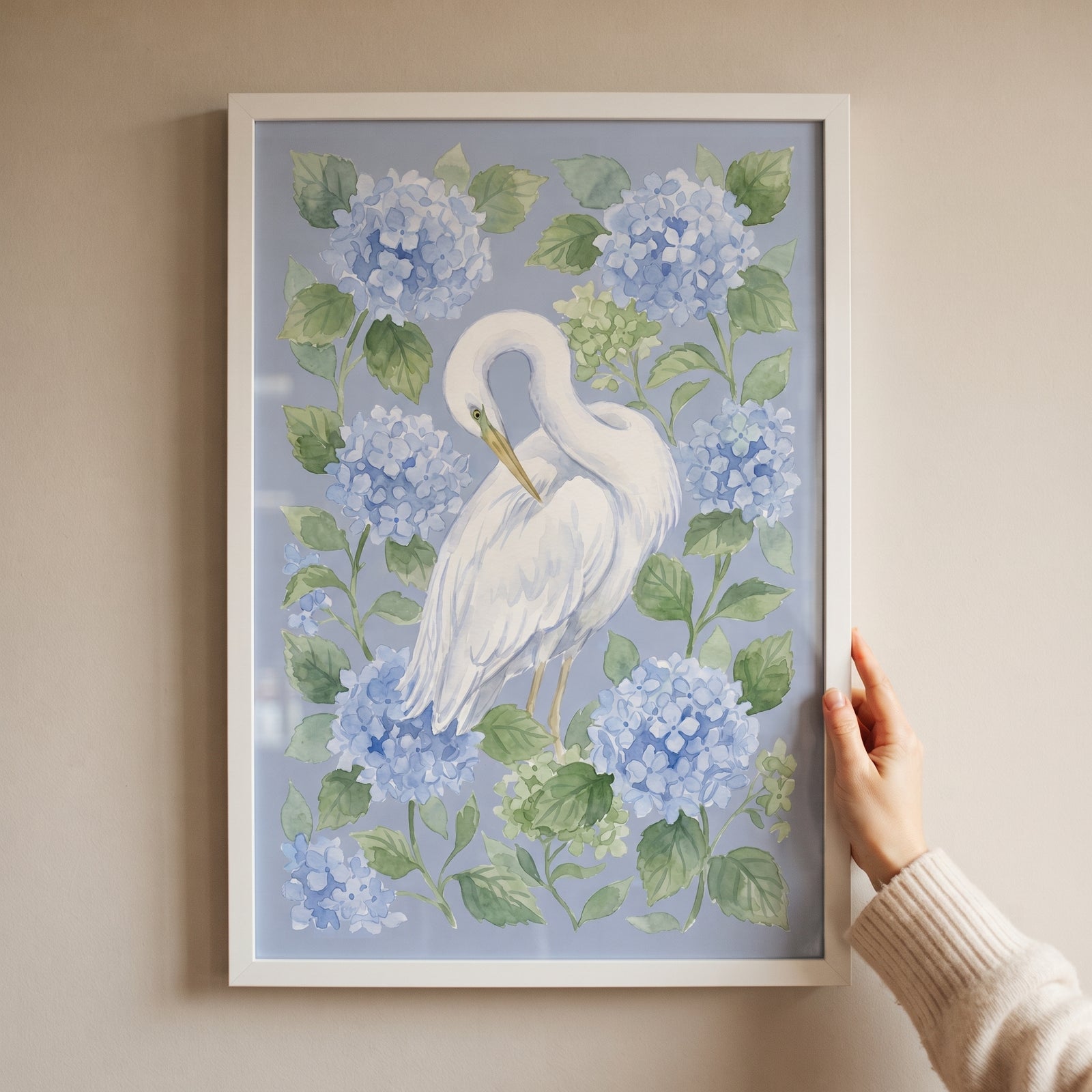 Hand holding framed blue hydrangea preening egret bird wall art with soft floral and avian details.