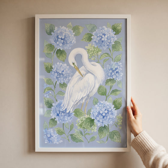 Hand holding framed blue hydrangea preening egret bird wall art with soft floral and avian details.