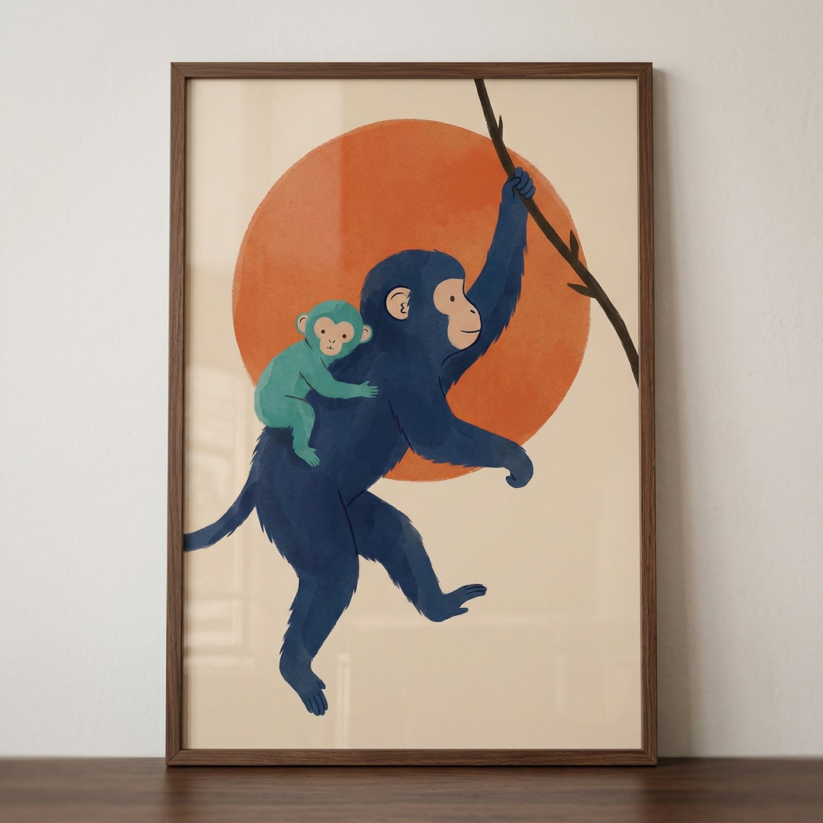 Framed illustration of a blue monkey swinging from a branch with a baby monkey holding onto its back in front of a large orange sun. The artwork sits on a wooden surface, creating a playful and warm jungle themed decor piece.