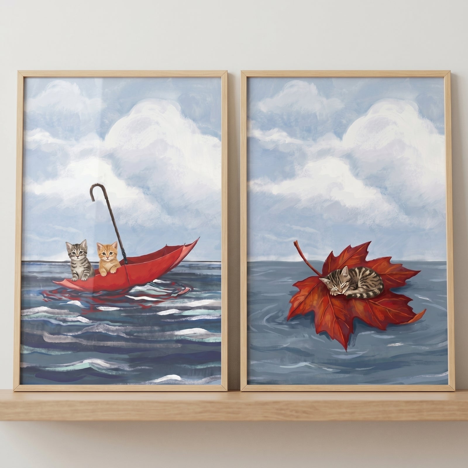 Blue ocean floating cat wall art set of 2 featuring kittens in a red umbrella and one asleep on a red leaf.