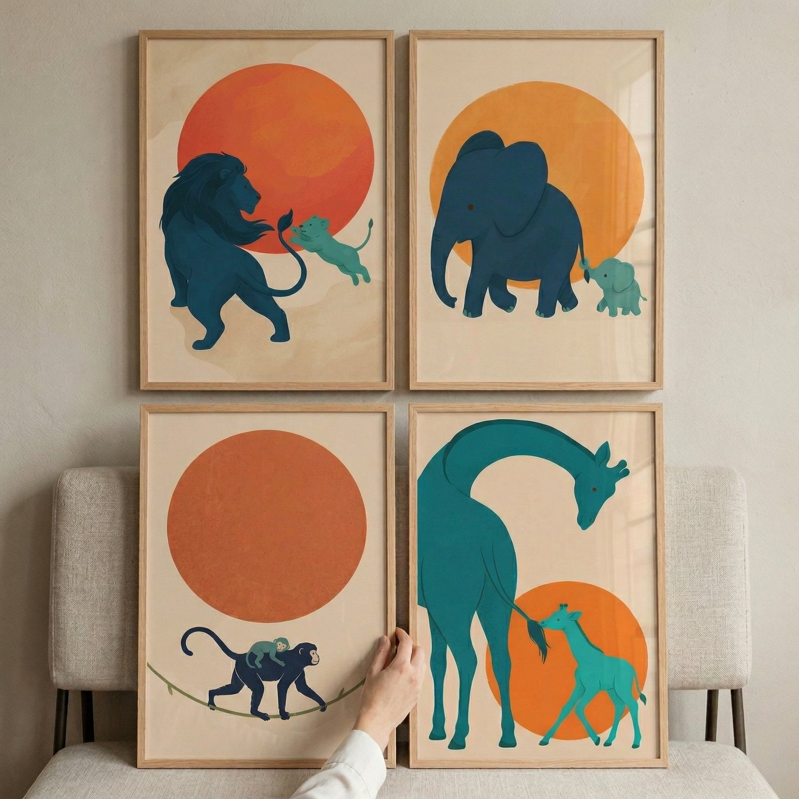 A set of four framed minimalist illustrations is displayed in a two-by-two grid on a neutral-colored wall. Each artwork features stylized animal silhouettes in dark blue and teal, depicting a parent and its young against the backdrop of a large, solid-colored sun.
