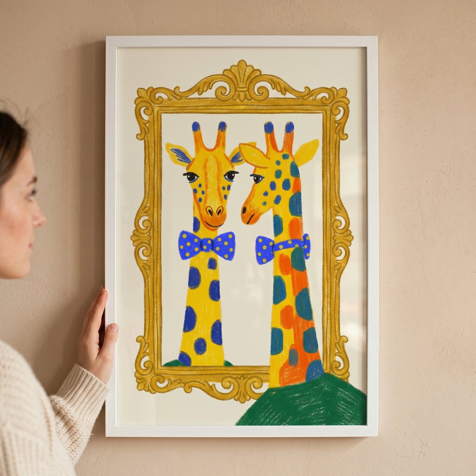 A woman holds framed blue polka dot giraffe wall art of a colorful giraffe wearing a bowtie looking into a gold mirror.