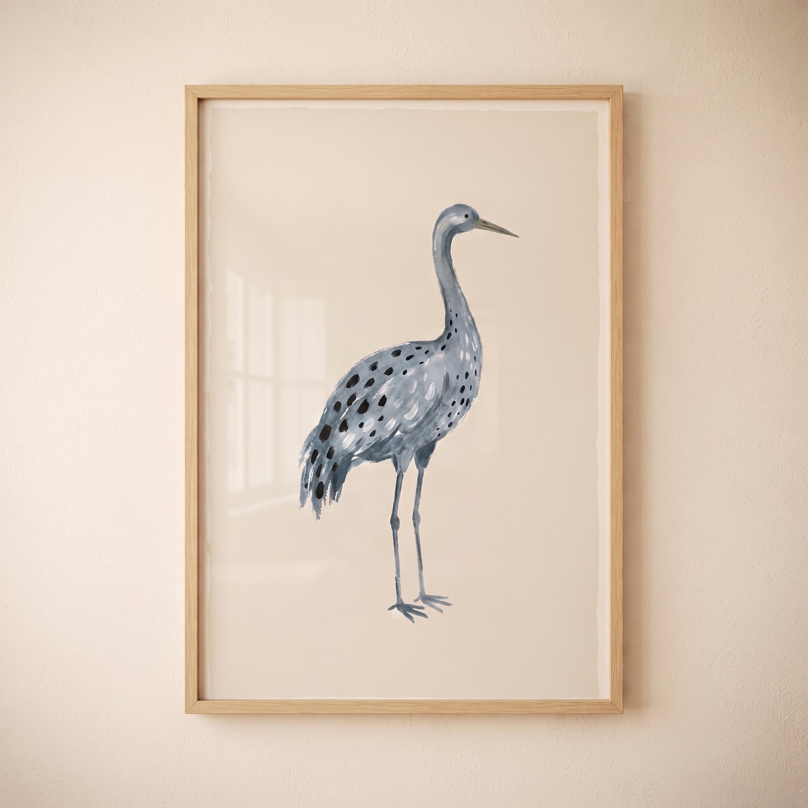 Blue spotted watercolor crane wall art in a light wood frame on a neutral beige wall.