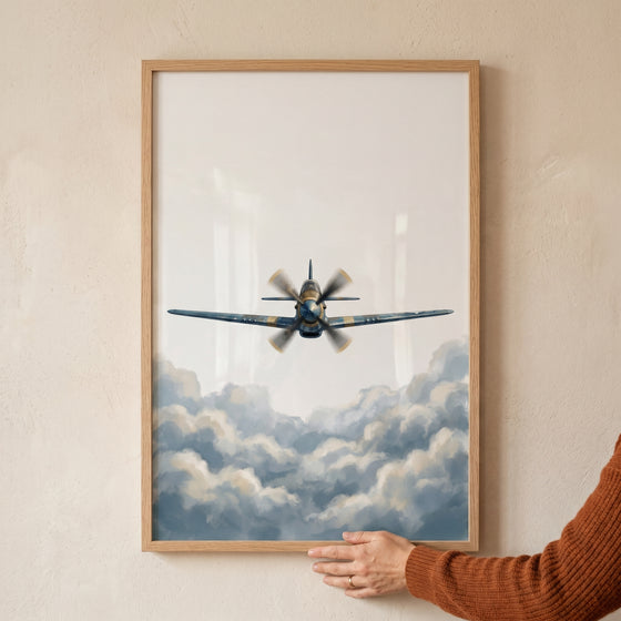 A hand holds a framed blue vintage clouds airplane wall art showing a propeller plane flying above soft clouds.
