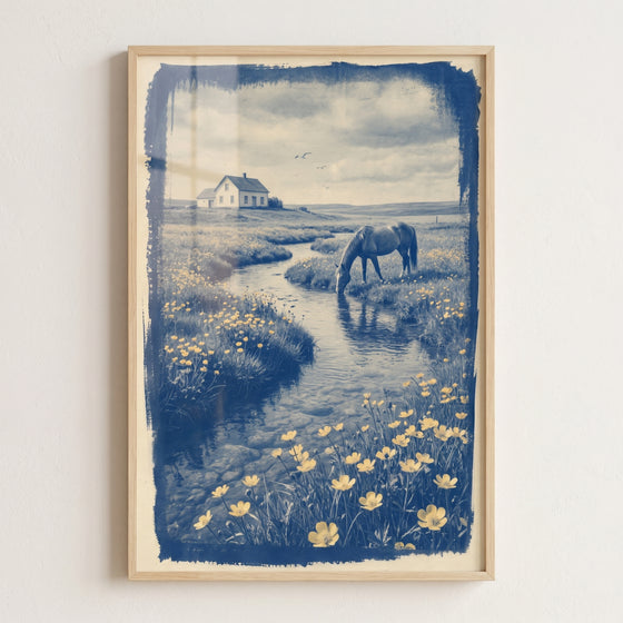 Framed blue vintage drinking horse wall art shows a horse at a stream in a field of yellow flowers near a house.