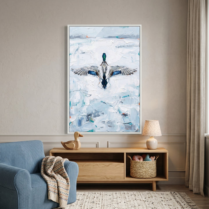 Blue wing landing mallard artwork displayed above a wooden console in a neutral room with a blue armchair and woven rug.