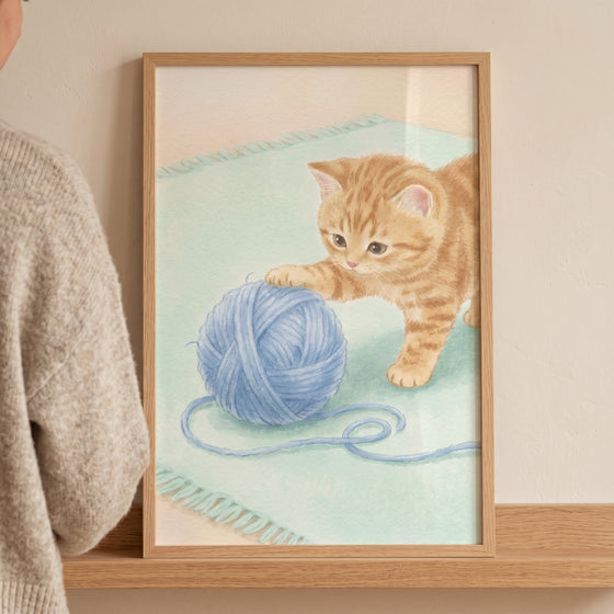 Orange tabby kitten playing with a blue ball of yarn on a light green rug in this blue yarn ball kitten artwork.