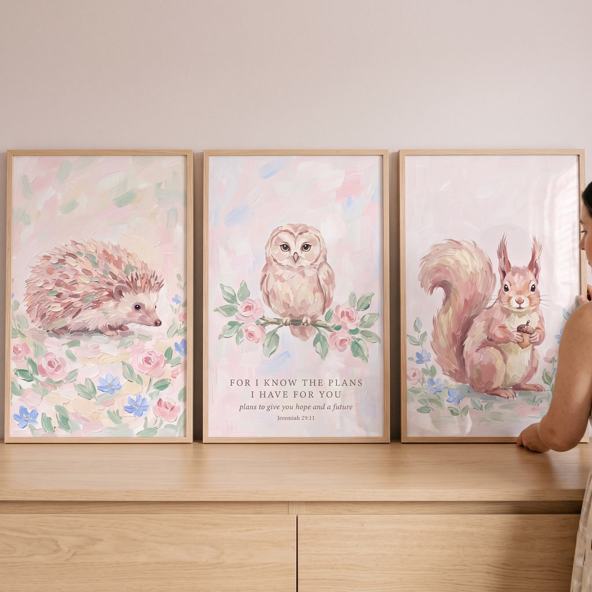 Blush bloom woodland animals wall art set of 3 with a hedgehog, owl, and squirrel on a light wood dresser.