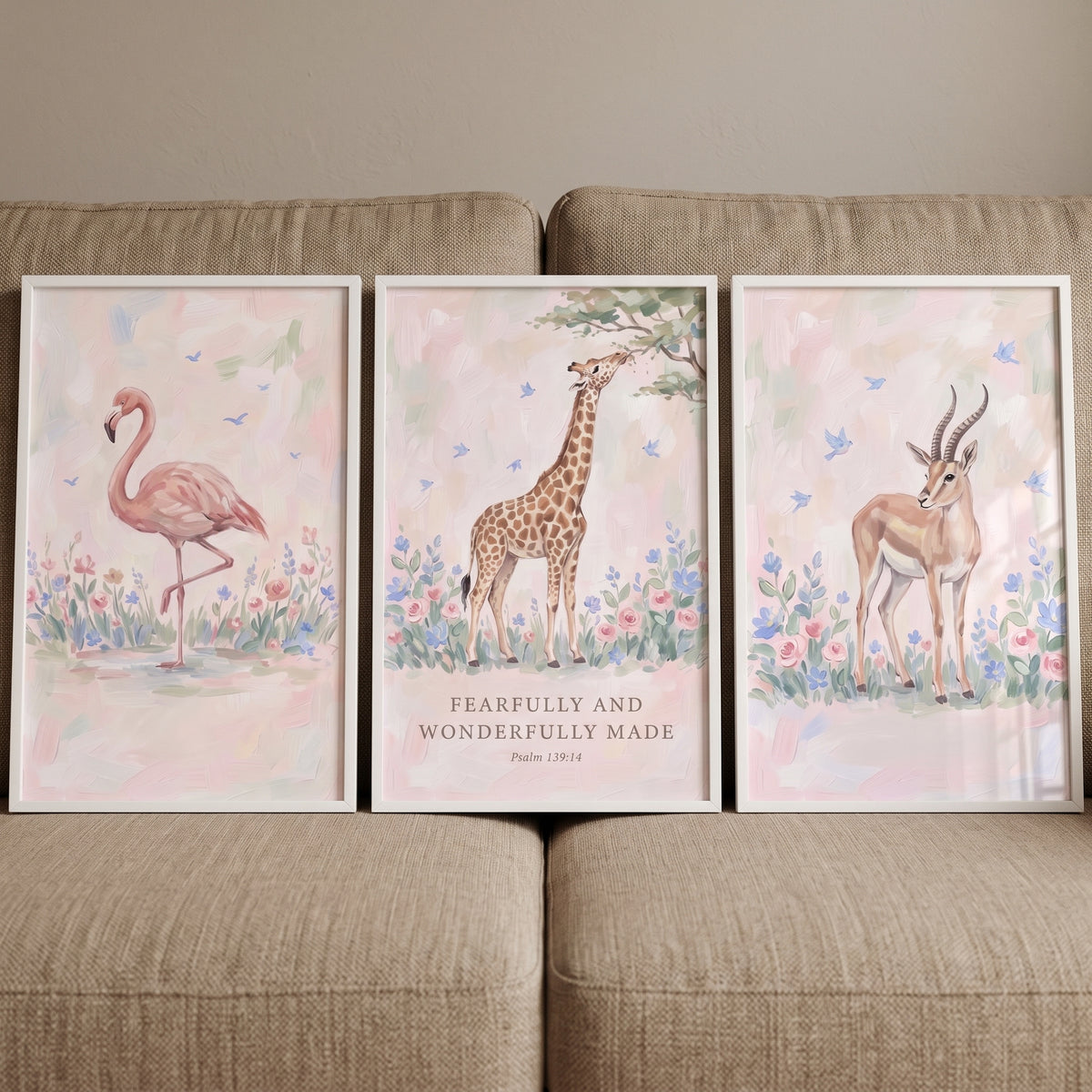 Blush botanical safari animals wall art set of 3 in white frames with a flamingo, giraffe, and gazelle on a tan couch.