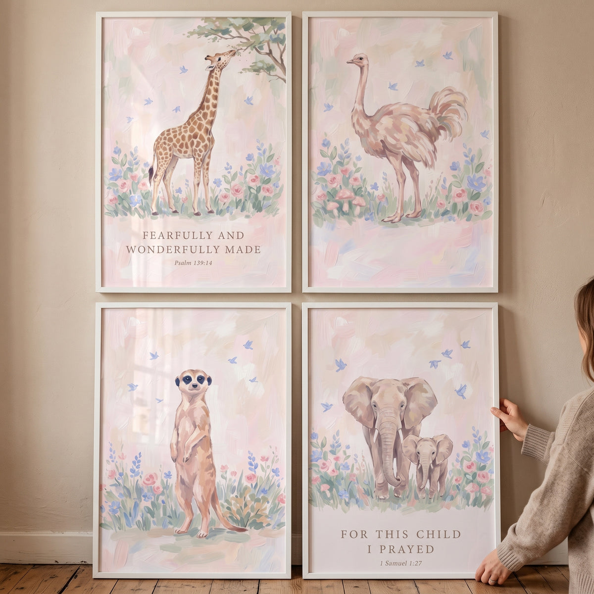 A person hangs a blush botanical savanna animals artwork set of 4 with a giraffe, ostrich, meerkat, and elephants.