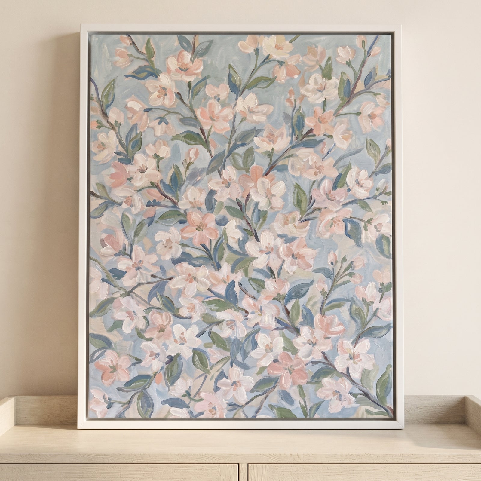 Blush pink cherry blossom floral wall art with green leaves on a light blue backdrop, displayed in a white frame.