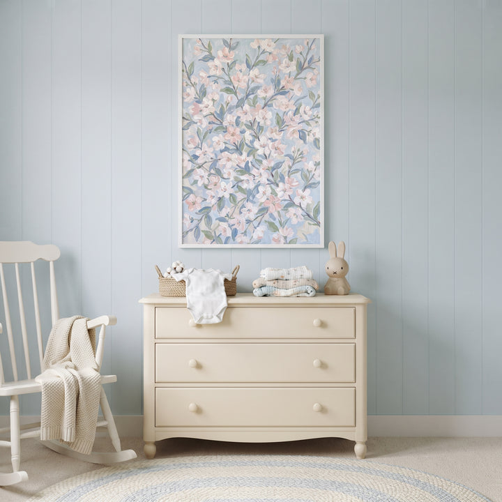 Blush pink cherry blossom floral wall art above a beige dresser and white rocking chair in a soft blue nursery.