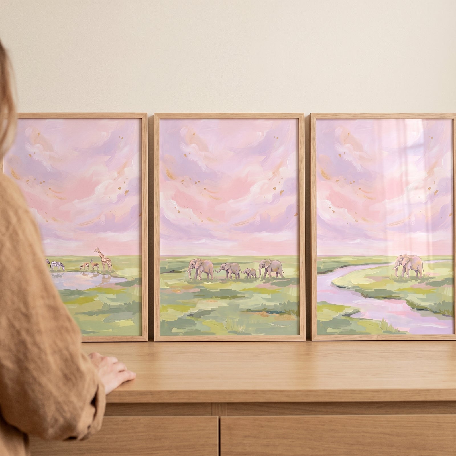 Framed blush pink safari animals wall art set of 3 features elephants and a giraffe under a soft pastel sky.