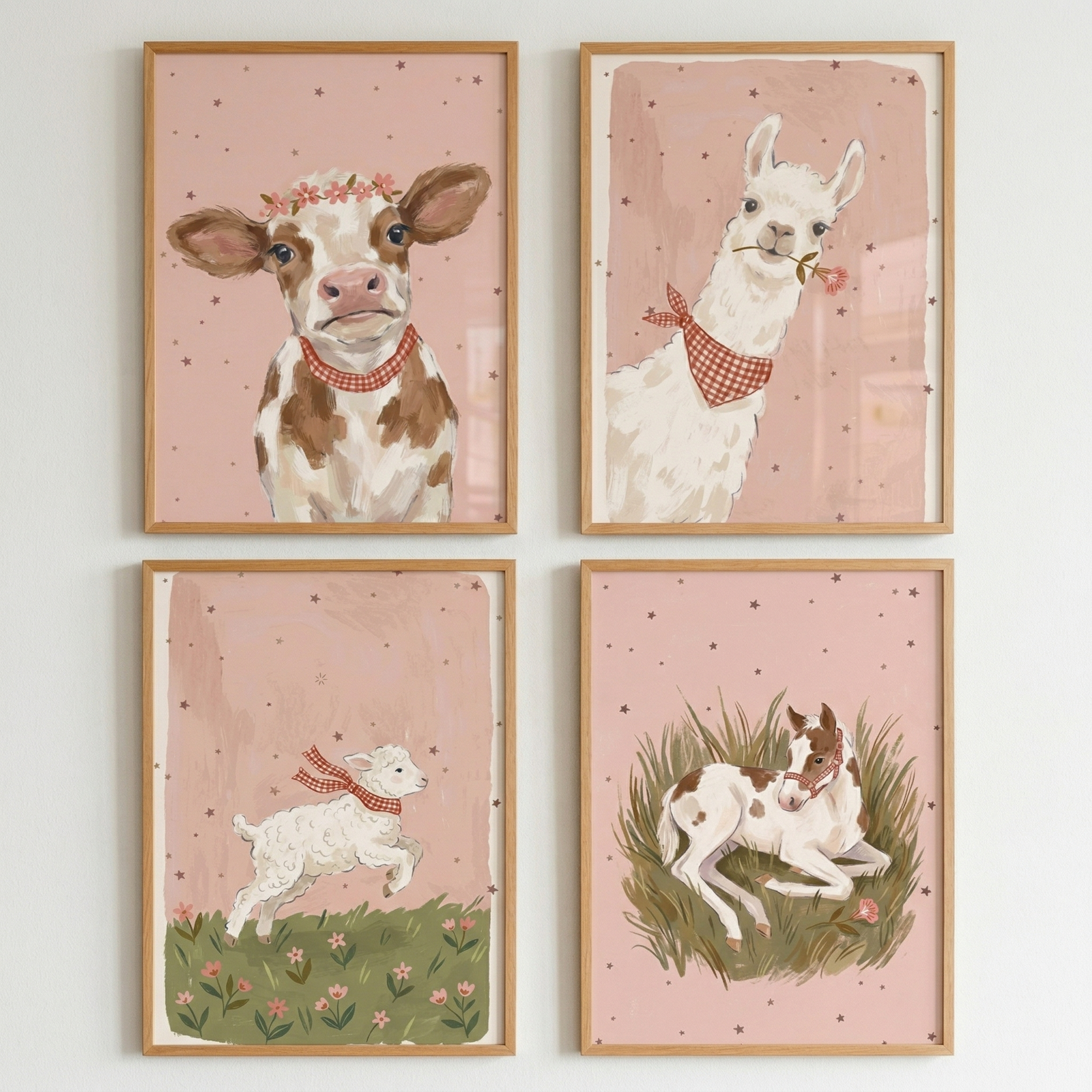 Four light-wood framed illustrations are arranged in a grid. Each features a whimsical animal on a pink, star-flecked background. Top-left: a brown and white calf in a flower crown and checkered bandana. Top-right: a white llama with a pink flower and red bandana. Bottom-left: a white lamb frolicking in a flowery green field. Bottom-right: a spotted brown and white foal resting in tall grass. The style is soft and illustrative, suitable for a nursery or child’s room.