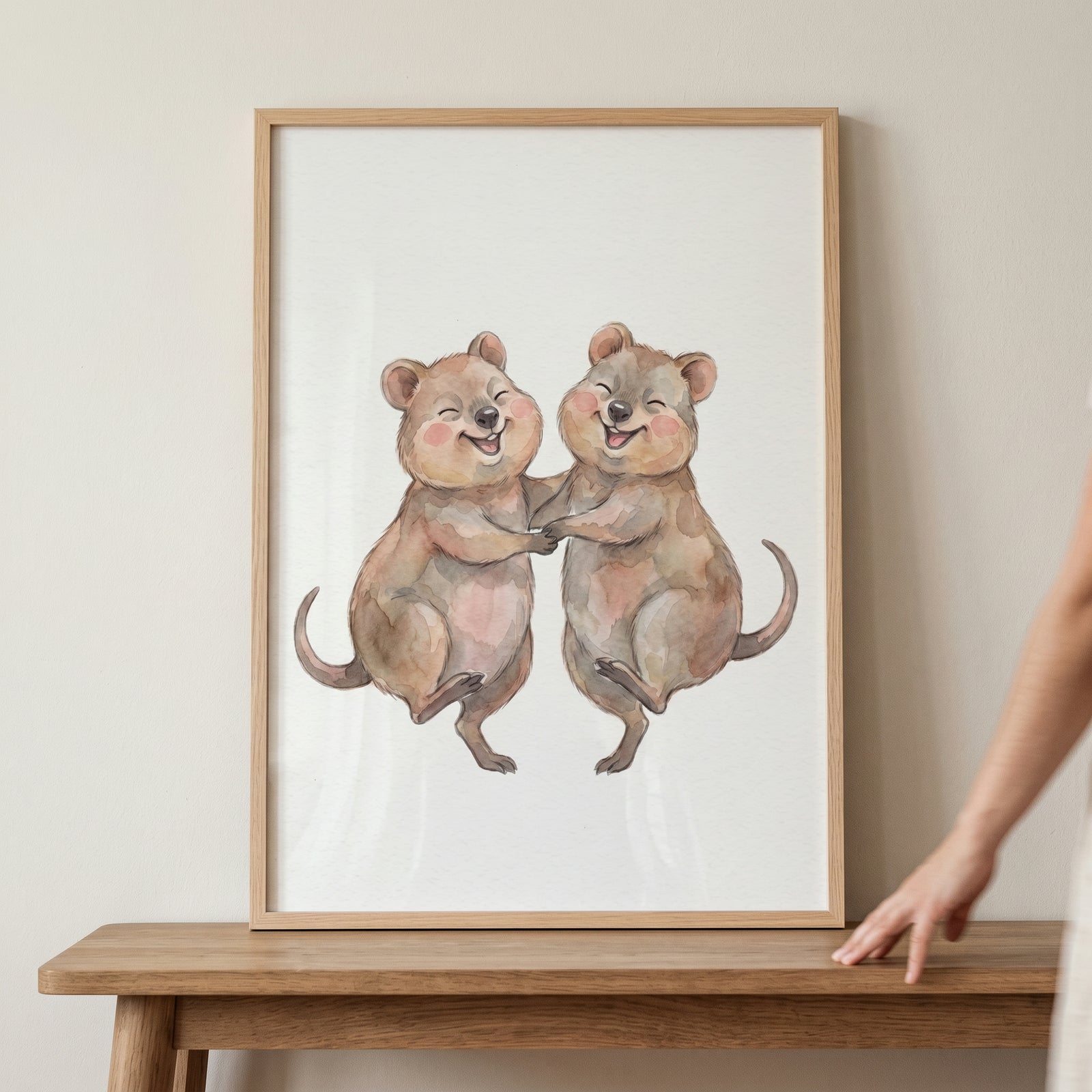 Blushing happy dancing quokka wall art in a light wood frame resting on a table.