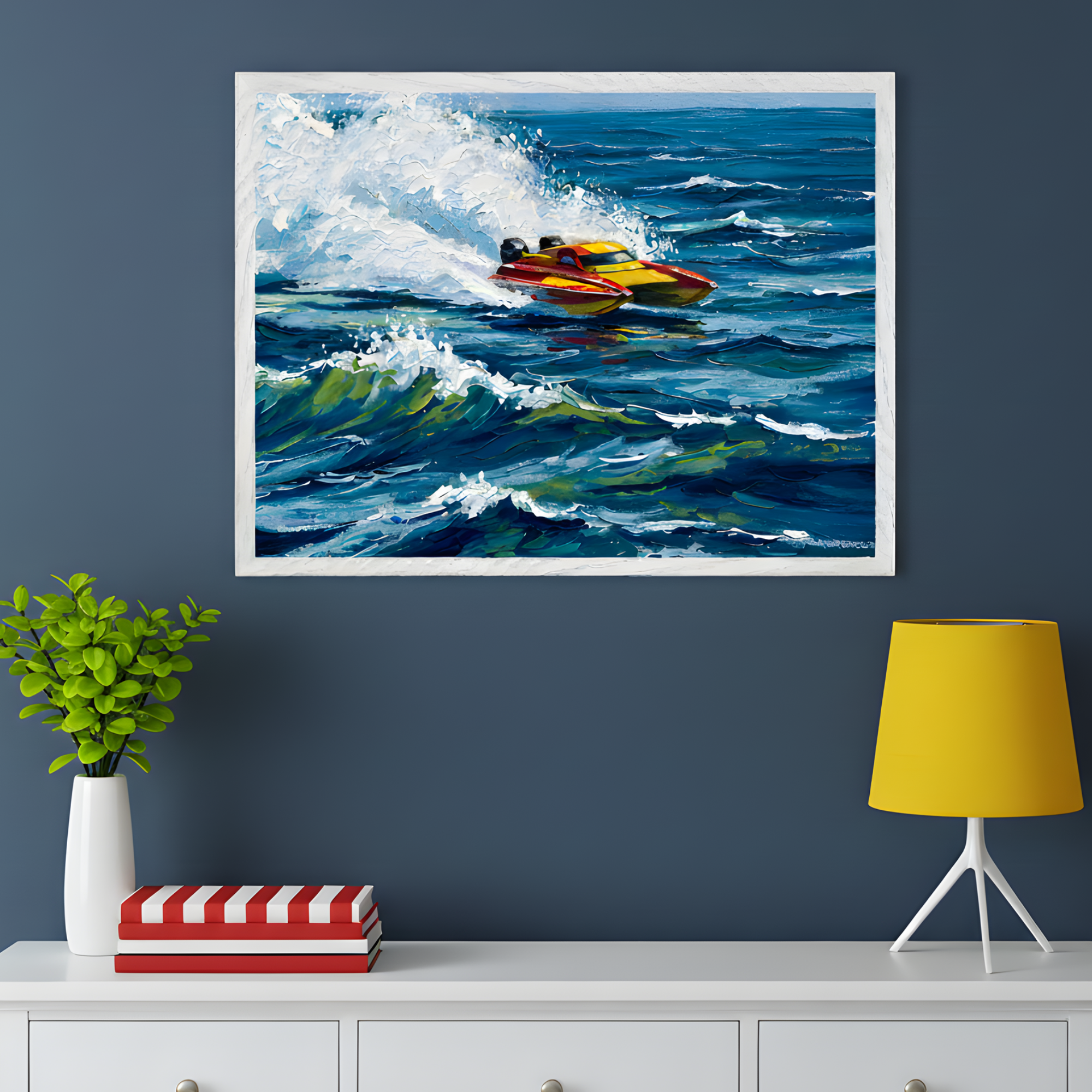 A framed artwork of a yellow and red speedboat racing through choppy blue ocean waves hangs on a dark blue wall. Below it, a white console table holds a small green plant in a white vase, two stacked red-and-white striped books, and a yellow lampshade, creating a bright and modern contrast.