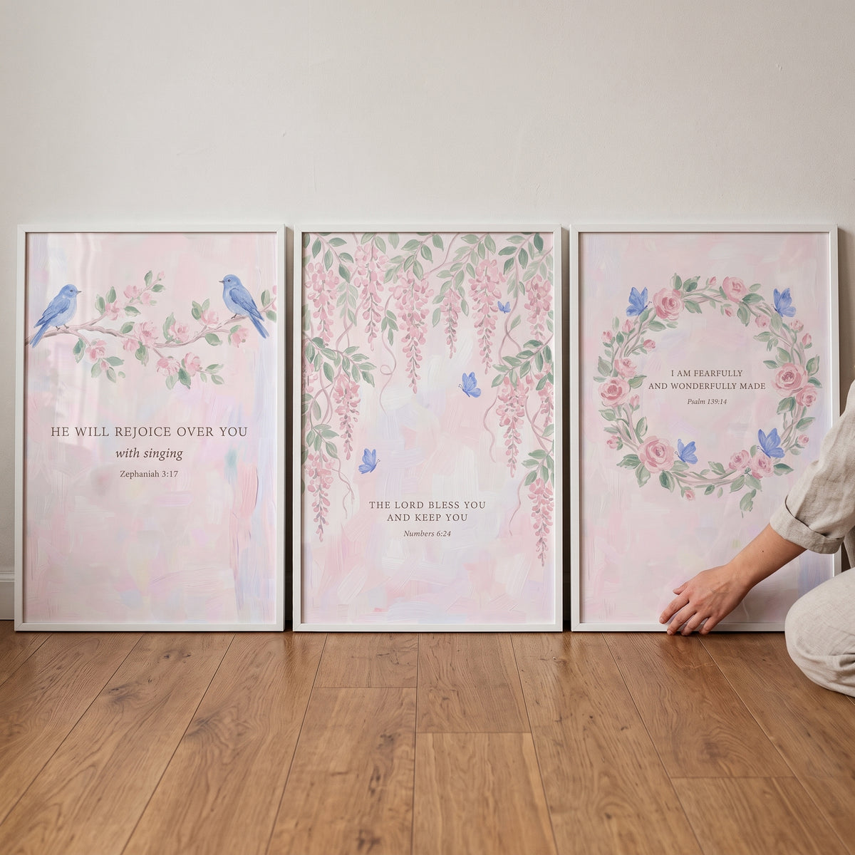 Botanical bible verse wall art set of 3 with floral designs and birds displayed in white frames on a wood floor.